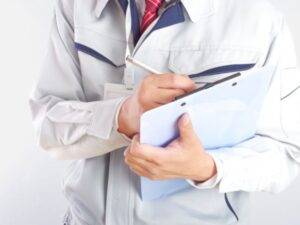 クリップボードへ真剣にペンを走らせる作業服の男性